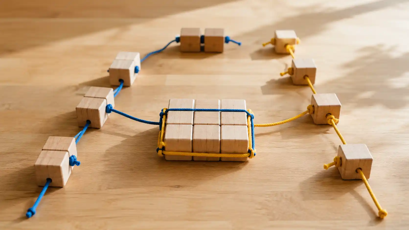 Bloques de madera organizados en patrones geométricos sobre una mesa de madera con cuerdas de colores, ilustrando visualmente los conceptos de MCM y MCD en matemáticas