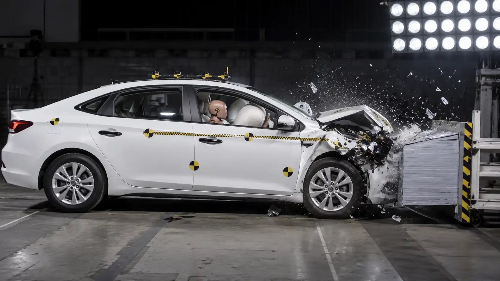 Crash test de automóvil blanco impactando barrera a alta velocidad con maniquí de prueba y marcadores amarillos