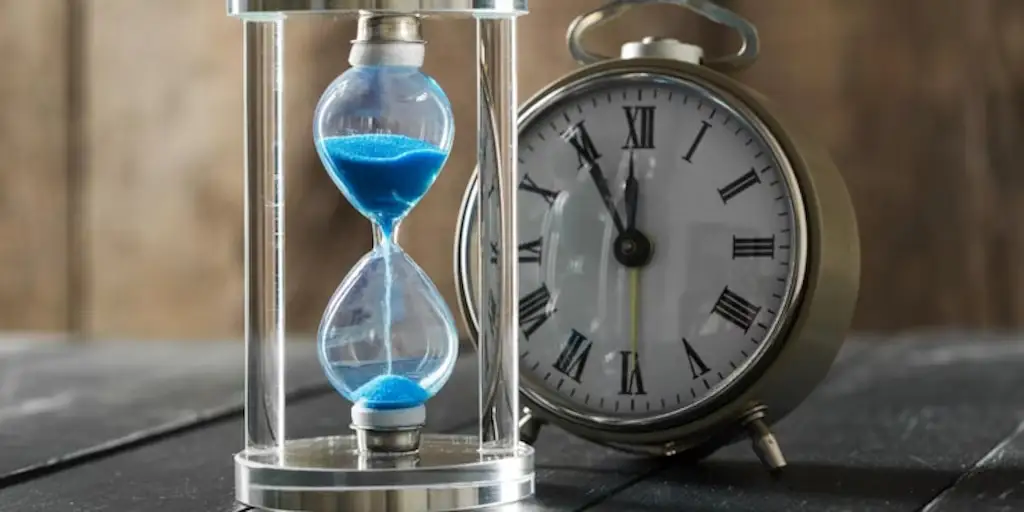 Reloj de arena con arena azul junto a reloj analógico vintage para calcular edad exacta en años meses y días